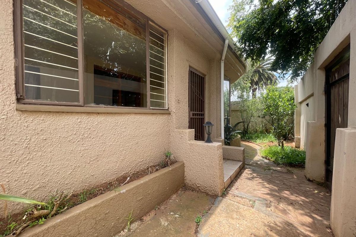 Exterior view of the side garden area featuring a paved walkway, textured wall finish, and security gate access to the property.