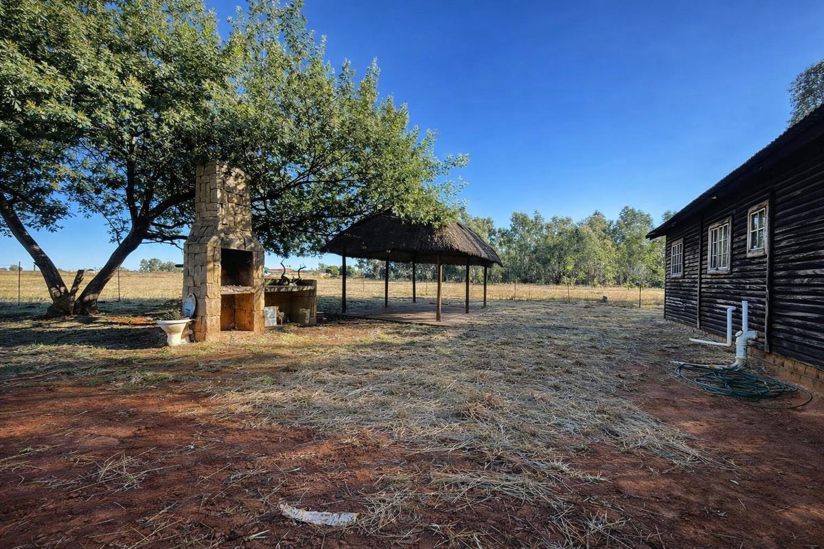 Outdoor area featuring a stone-built braai, a thatched gazebo, and rustic timber-clad building exterior set in a rural landscape.