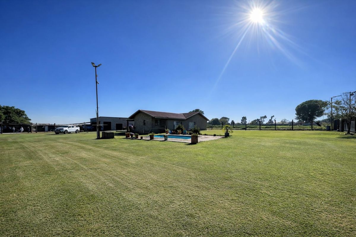 A wide-angle view of the property exterior featuring a large lawn, a swimming pool, and the main house structure under a clear sky.