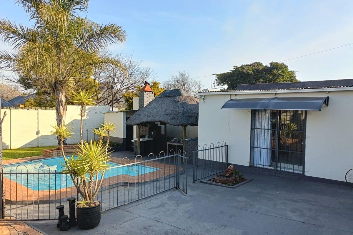 Rear exterior view featuring a swimming pool, a thatched lapa with a built-in braai, and a paved patio area.