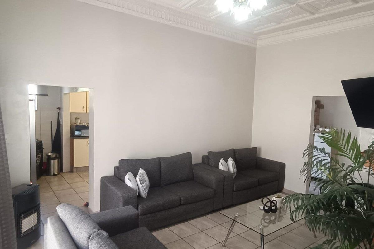 A living room featuring tiled flooring, decorative ceiling tiles with cornice, and a built-in gas heater, with an adjacent view into the kitchen area.