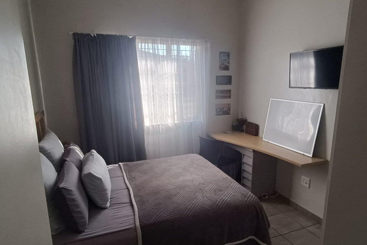 A functional bedroom featuring tiled flooring, a built-in desk workspace, and a window fitted with security bars.