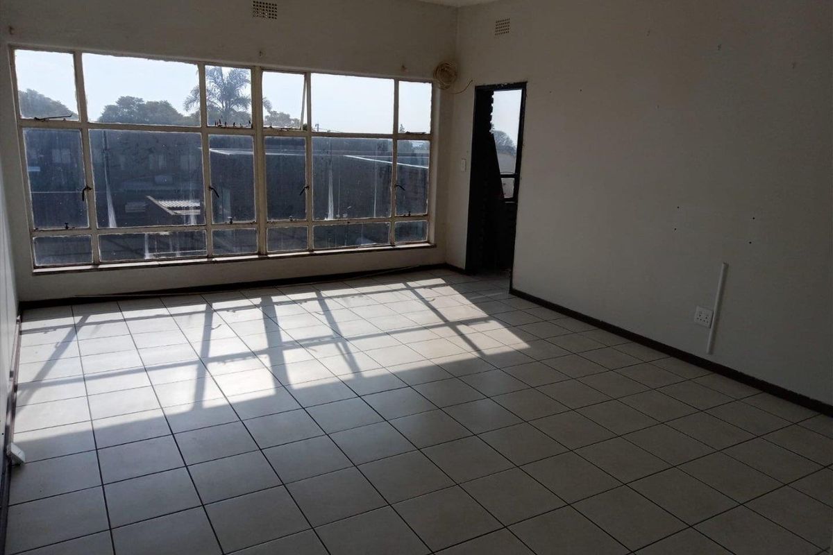 An empty, sunlit living area featuring large metal-framed windows and ceramic tiled flooring, offering a blank canvas for renovation.