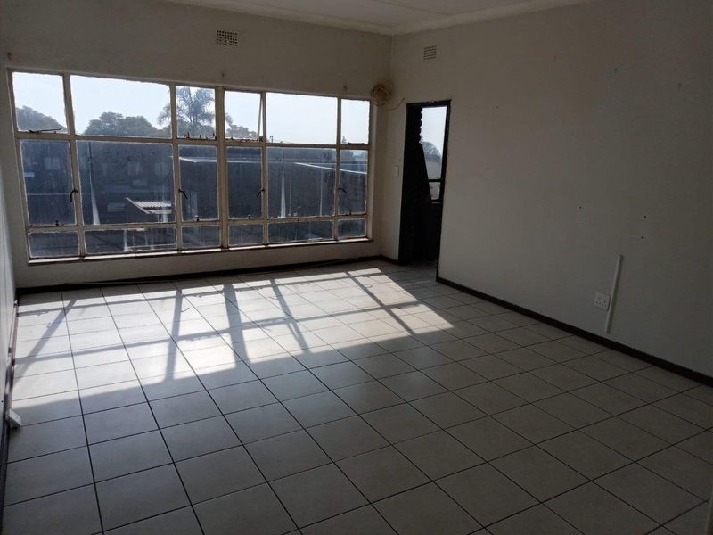 An empty, sunlit living area featuring large metal-framed windows and ceramic tiled flooring, offering a blank canvas for renovation.