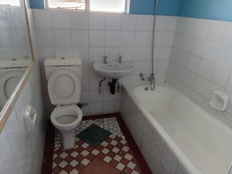 A functional bathroom featuring a standard bathtub, wall-mounted basin, and toilet with tiled walls and flooring, offering potential for modern renovation.