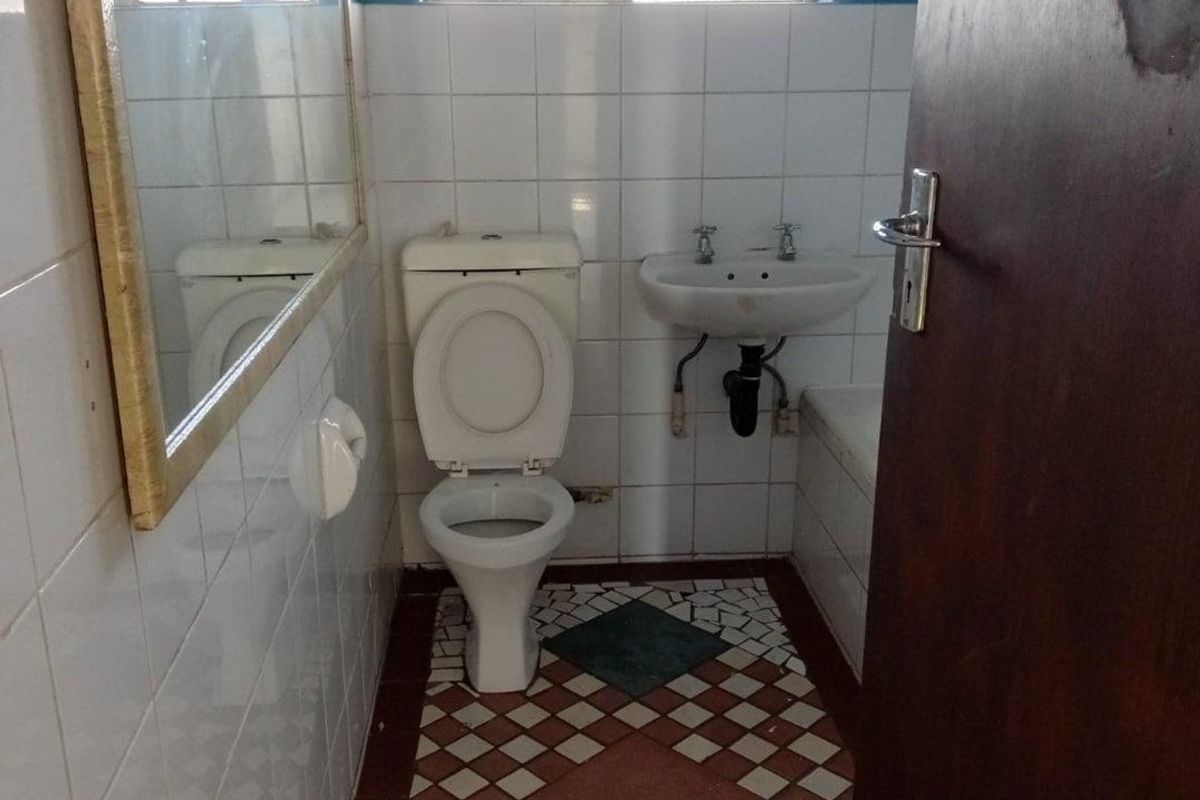 A compact bathroom featuring a toilet, wall-mounted basin, and tiled finishes. The space is functional but would benefit from modern updates.