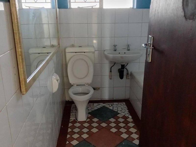A compact bathroom featuring a toilet, wall-mounted basin, and tiled finishes. The space is functional but would benefit from modern updates.