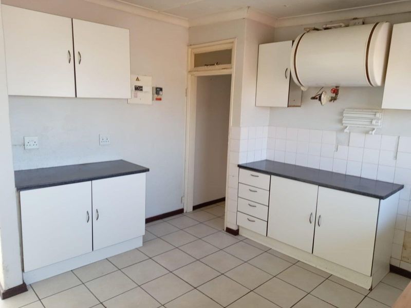 A functional kitchen space featuring white built-in cabinetry, dark laminate countertops, tiled flooring, and an exposed electric water heater.