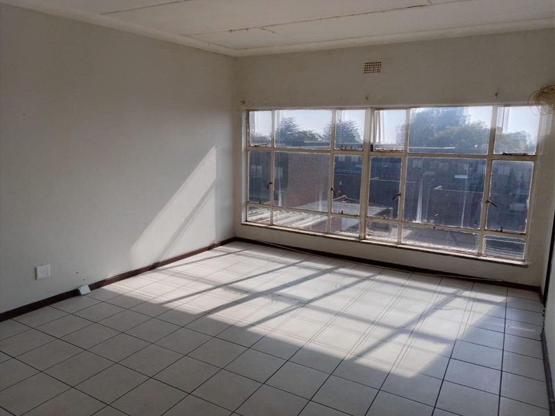 An empty, sunlit living area featuring tiled flooring and large steel-framed windows, offering a blank canvas for renovation and interior design.