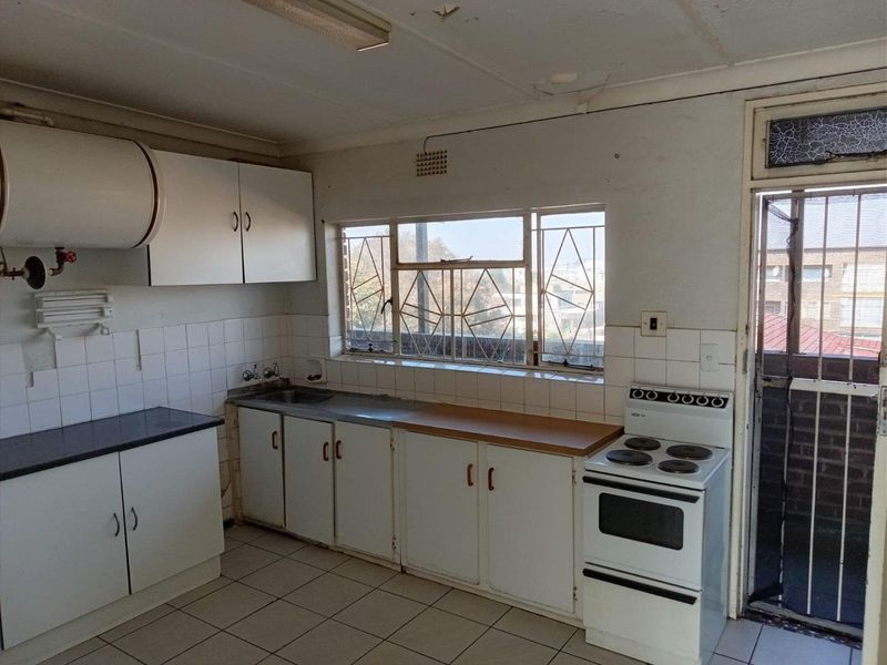 A dated kitchen featuring built-in cabinetry, tiled flooring, and a stainless steel sink, requiring cosmetic updates and repairs to the ceiling and window.