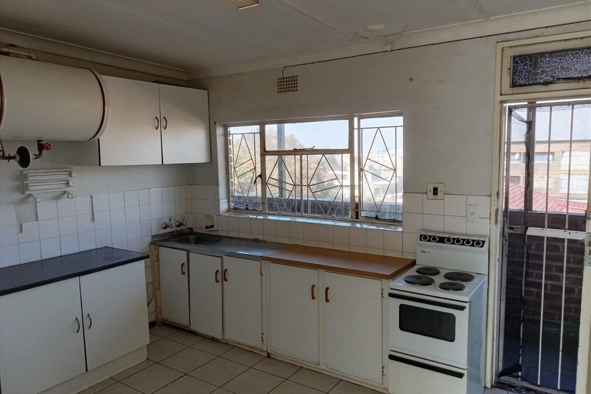 A dated kitchen featuring built-in cabinetry, tiled flooring, and a stainless steel sink, requiring cosmetic updates and repairs to the ceiling and window.