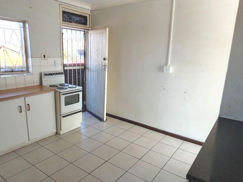 A functional kitchen space featuring tiled flooring, a laminate countertop, and a freestanding stove, with direct access to an exterior door.