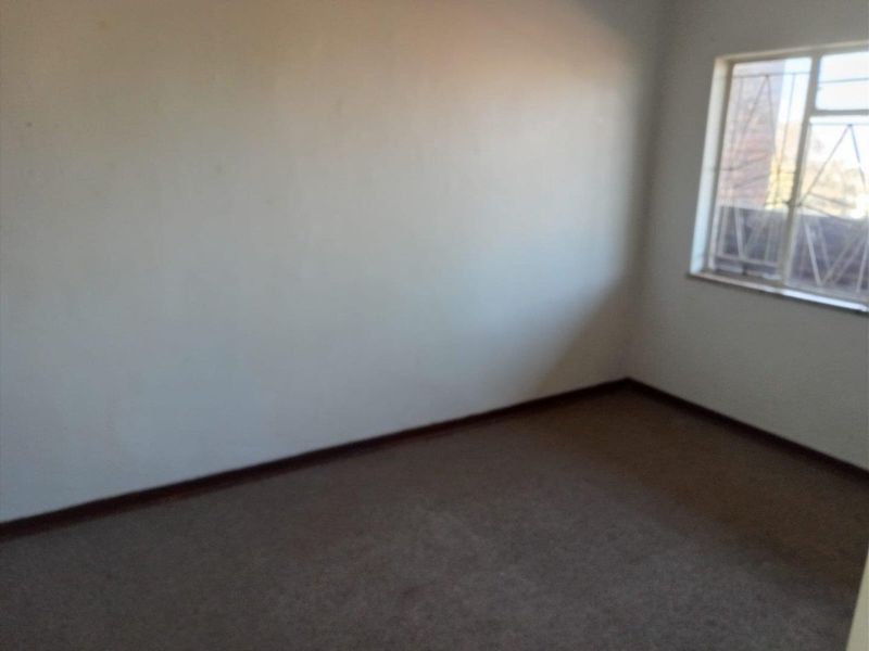 An empty bedroom featuring carpet flooring and a window fitted with security bars, offering a blank canvas for potential renovation.