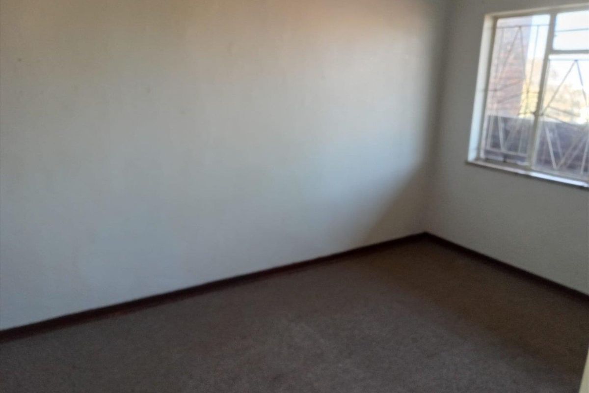 An empty bedroom featuring carpet flooring and a window fitted with security bars, offering a blank canvas for potential renovation.