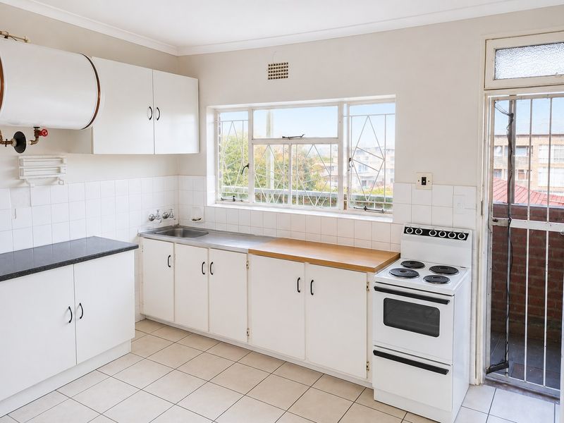 A functional kitchen featuring white cabinetry, tiled splashbacks, a stainless steel sink, and a freestanding electric stove, with direct access to an outdoor area.