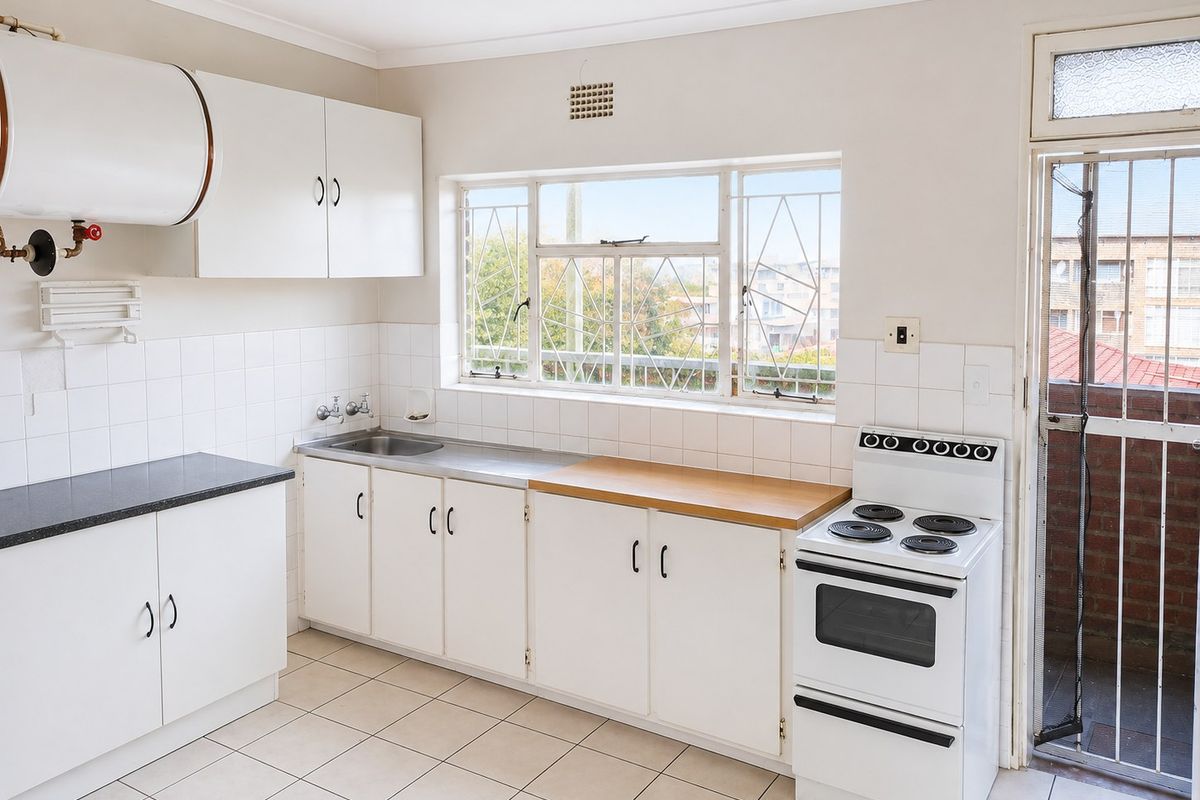 A functional kitchen featuring white cabinetry, tiled splashbacks, a stainless steel sink, and a freestanding electric stove, with direct access to an outdoor area.