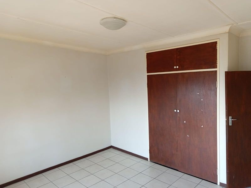 An empty bedroom featuring tiled flooring and built-in wooden cupboards with some visible wear and tear.