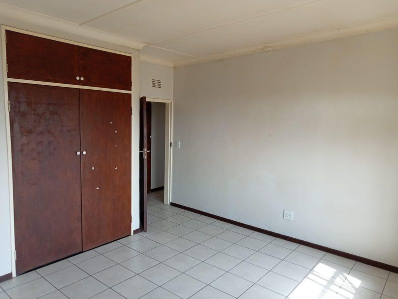 An empty bedroom featuring built-in wooden cupboards, ceramic tiled flooring, and neutral walls, offering a blank canvas for renovation or staging.