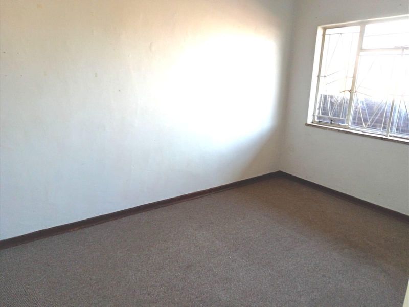 An empty bedroom featuring carpeted flooring, plain walls, and a window fitted with security bars.