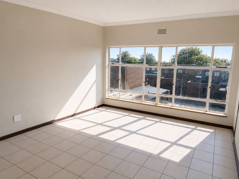 A bright, empty bedroom featuring neutral tiled flooring and a large multi-pane window providing ample natural light and an urban view.