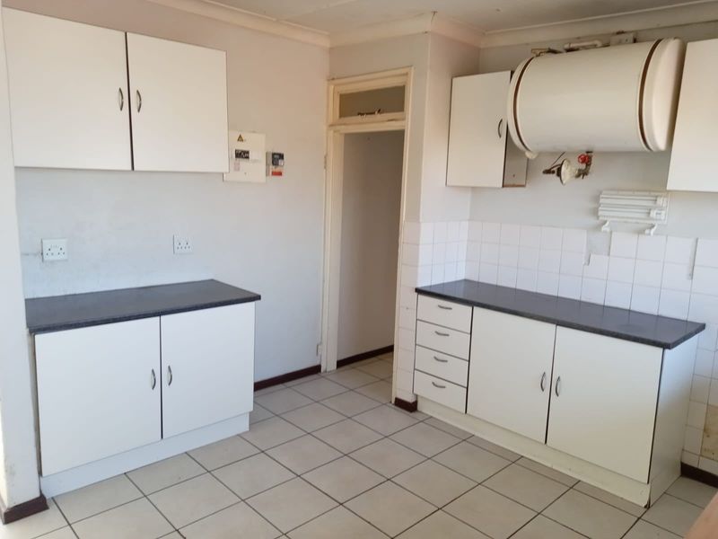 A functional kitchen space featuring white cabinetry, laminate countertops, tiled flooring, and an exposed electric water heater, ready for modernization.