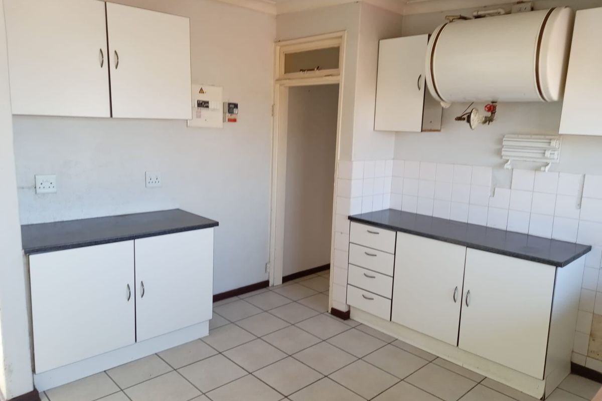 A functional kitchen space featuring white cabinetry, laminate countertops, tiled flooring, and an exposed electric water heater, ready for modernization.