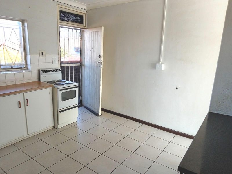 A functional, empty kitchen featuring tiled flooring, built-in cabinetry, and a freestanding stove, with direct access to an exterior door.