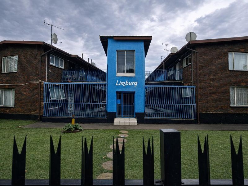 Front elevation of the Limburg apartment complex featuring brick construction, blue accent facade, and secure perimeter fencing.