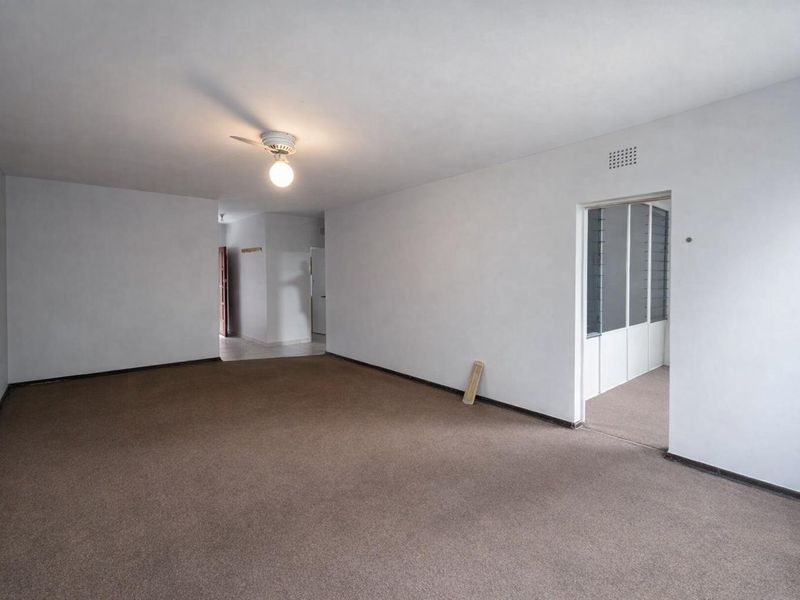 A spacious, empty living area featuring neutral walls, carpet flooring, and a ceiling fan, offering a blank canvas for interior design.