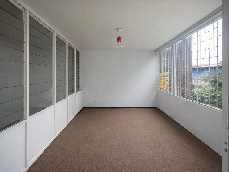 An empty living area featuring carpet flooring, louvered windows, and security bars, offering a blank canvas for interior design.