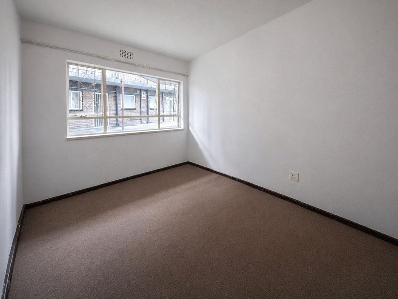 An empty bedroom featuring carpet flooring, a window with security bars, and neutral walls, offering a blank canvas for personalization.