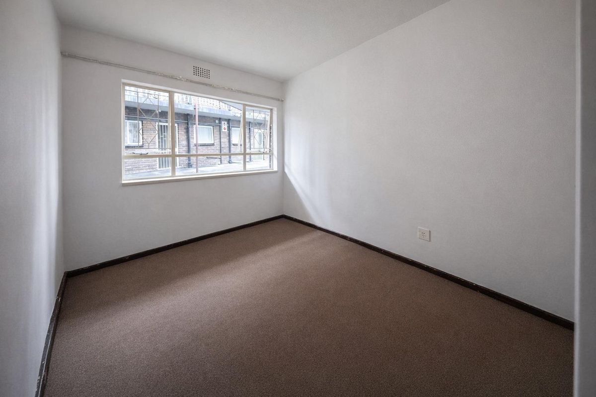 An empty bedroom featuring carpet flooring, a window with security bars, and neutral walls, offering a blank canvas for personalization.