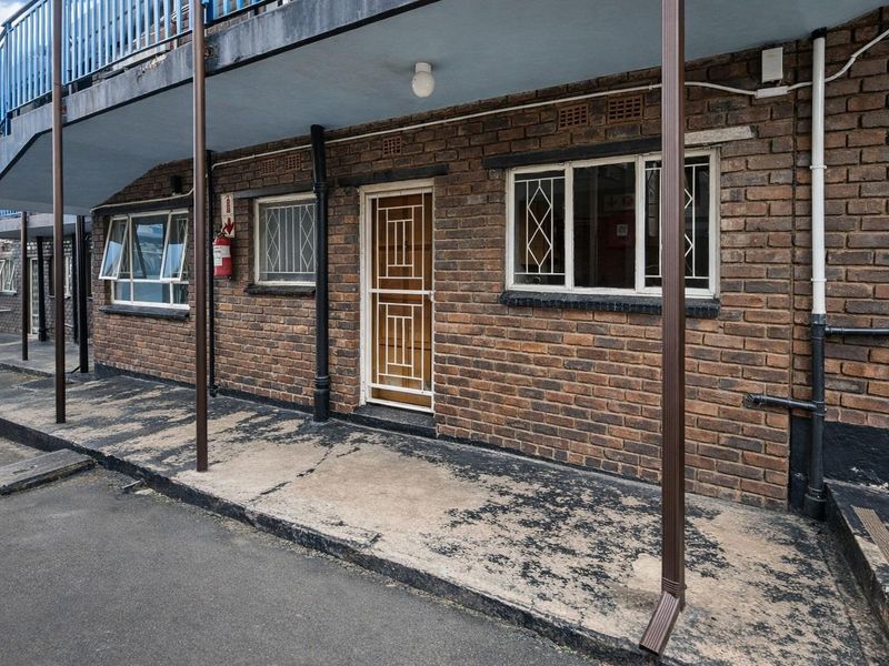 Exterior view of an apartment unit featuring exposed brickwork, a security gate, and a covered walkway area with visible surface wear.