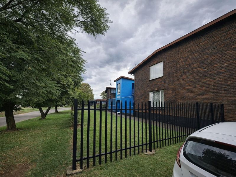 Exterior view of a brick apartment building featuring secure metal perimeter fencing and established surrounding greenery.