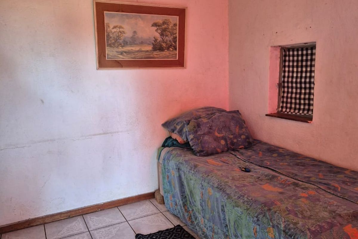 A compact bedroom featuring ceramic floor tiles and a small window, currently requiring cosmetic updates to the wall finishes.