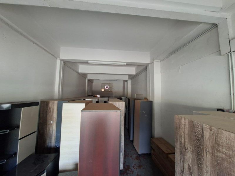 A utilitarian commercial storage or workspace featuring exposed structural beams, functional lighting, and a ventilation fan, currently used for inventory storage.