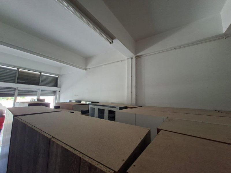 A functional utility or storage space featuring high ceilings, fluorescent lighting, and aluminium window frames with integrated roller shutters.