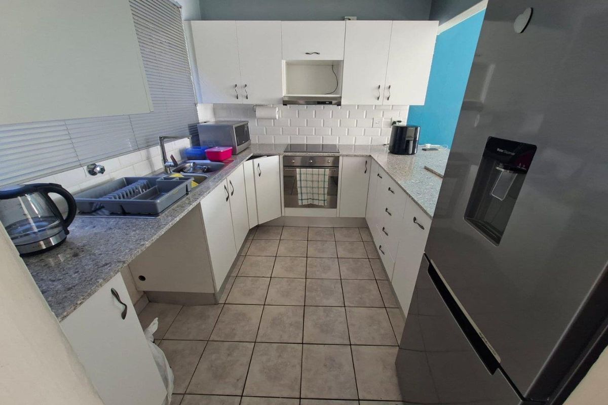 A functional kitchen featuring white cabinetry, granite-look countertops, a built-in oven with extractor fan, and tiled flooring.