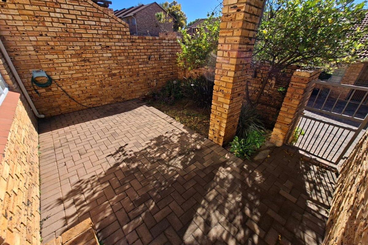 A private paved courtyard featuring exposed brick walls, a brick pillar, and a secure metal gate entrance.