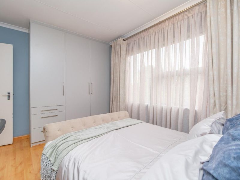 A well-maintained bedroom featuring light wood flooring, built-in floor-to-ceiling cabinetry, and large windows with neutral curtains.