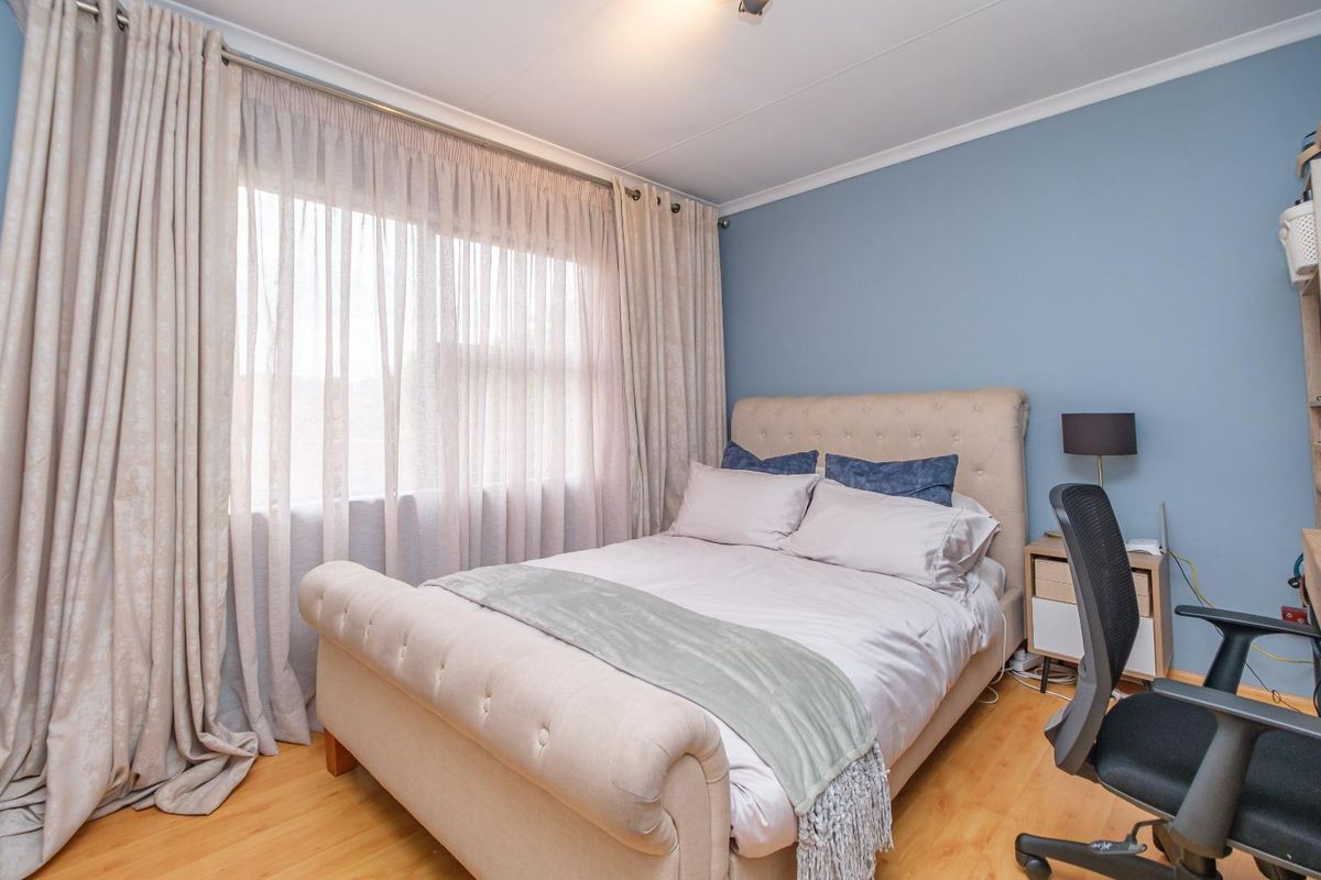 A well-lit bedroom featuring light wood-look flooring, blue accent wall, and large window with floor-to-ceiling curtains.