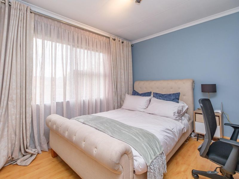 A well-lit bedroom featuring light wood-look flooring, blue accent wall, and large window with floor-to-ceiling curtains.