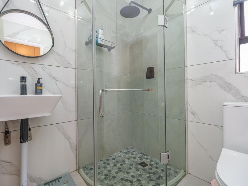 Modern bathroom featuring a glass-enclosed shower with rainfall showerhead, marble-look wall tiles, a wall-mounted basin, and a contemporary toilet.