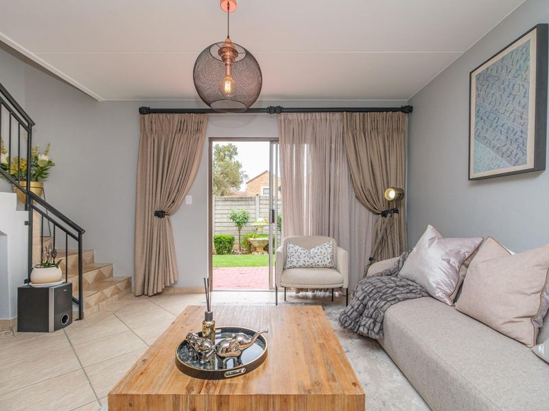 A well-maintained living room featuring tiled flooring, a staircase with a metal railing, and sliding glass doors providing access to the rear garden.