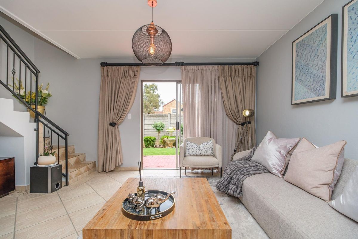 A well-maintained living room featuring tiled flooring, a staircase with a metal railing, and sliding glass doors providing access to the rear garden.