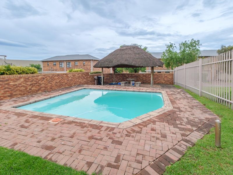 Outdoor pool area featuring a paved surround, brick boundary wall, and a thatched lapa structure for shaded seating.
