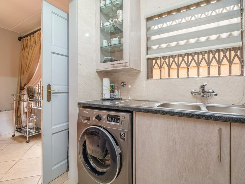A functional laundry area featuring built-in cabinetry, a stainless steel sink with mixer tap, and space for a washing machine.