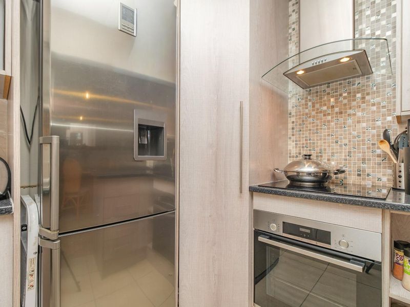 Modern kitchen featuring built-in stainless steel oven, glass extractor fan, and mosaic tile backsplash with integrated cabinetry.