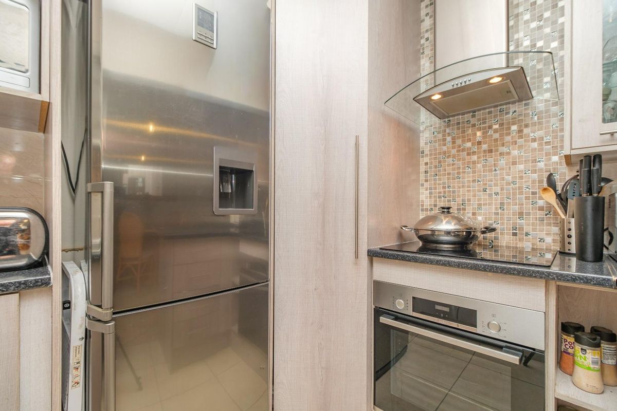 Modern kitchen featuring built-in stainless steel oven, glass extractor fan, and mosaic tile backsplash with integrated cabinetry.