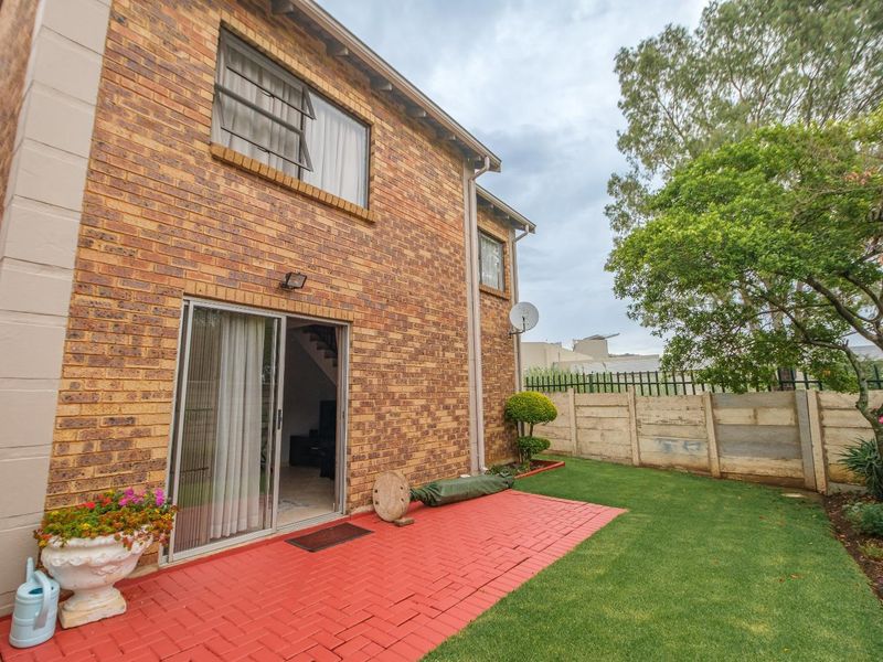 Rear view of the townhouse featuring a red brick facade, sliding glass door access, a paved patio area, and a private garden with boundary wall.